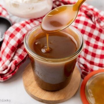 Spoon dipped in butterscotch sauce with some drizzling off of it into the jar.