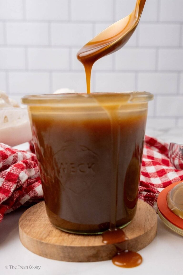 Side view of butterscotch syrup in a jar with a spoon taking some.