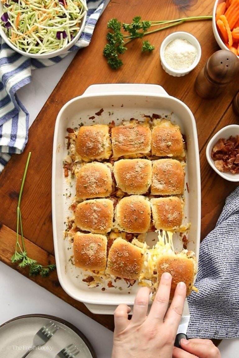 Hand puling a chicken bacon ranch slider from the rest of them in a baking dish.