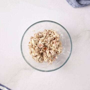 Chicken mixed with ranch and bacon in a mixing bowl.