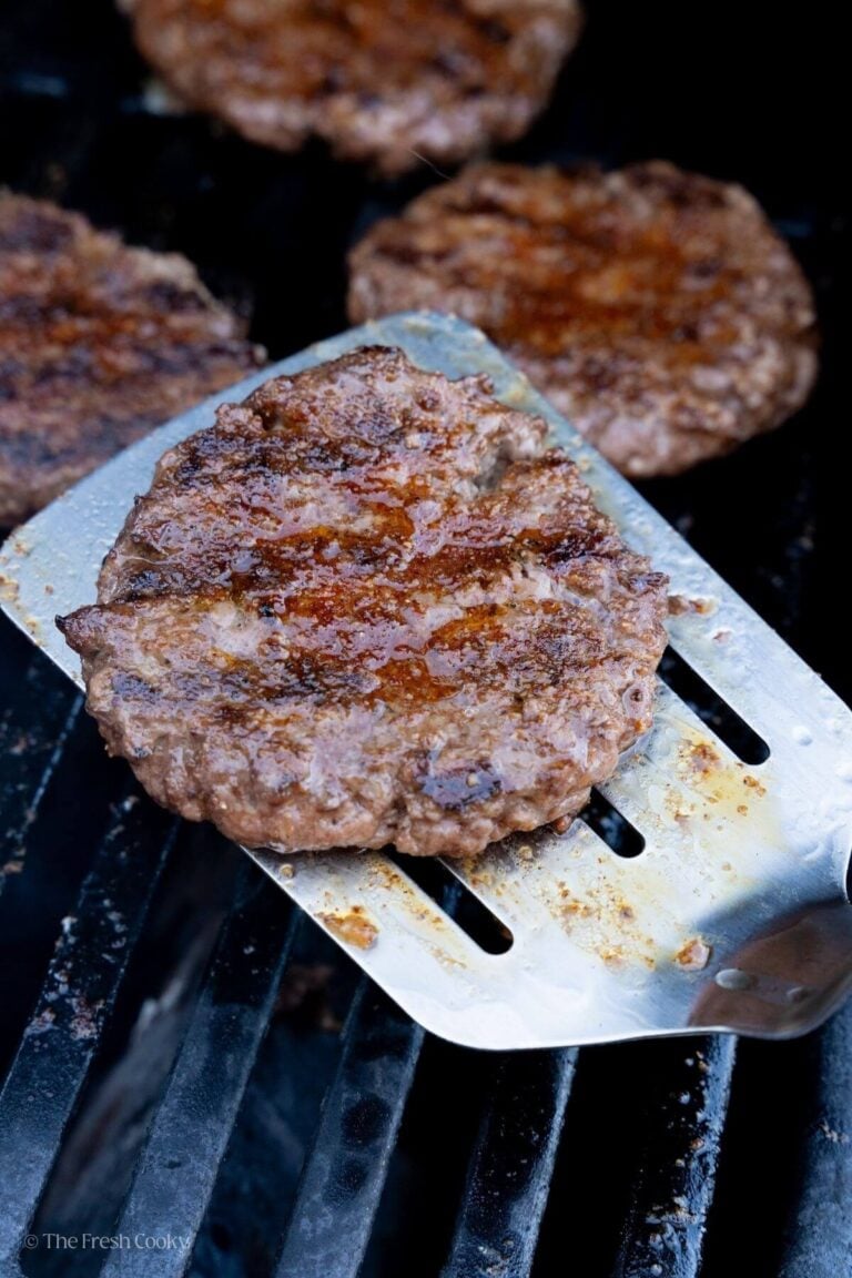 Metal spatula with a hamburger patty on it with the grill grates underneath.