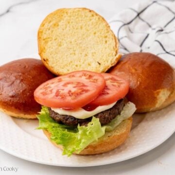 Burger being assembled with toppings on a plate.