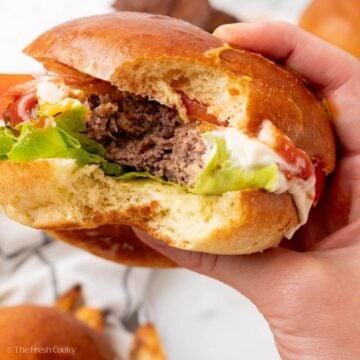 Hand holding a burger with a bite taken out of it.