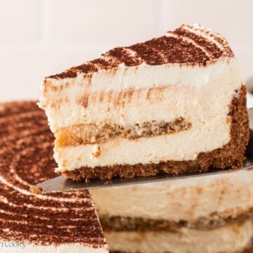 Slice of tiramisu cake on a metal spatula hovering over the rest of the cake.