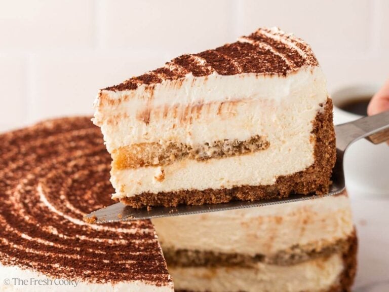 Slice of tiramisu cake on a metal spatula hovering over the rest of the cake.