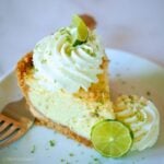Slice of key lime pie decorated with swirls of thick whipped cream and slices of lime.