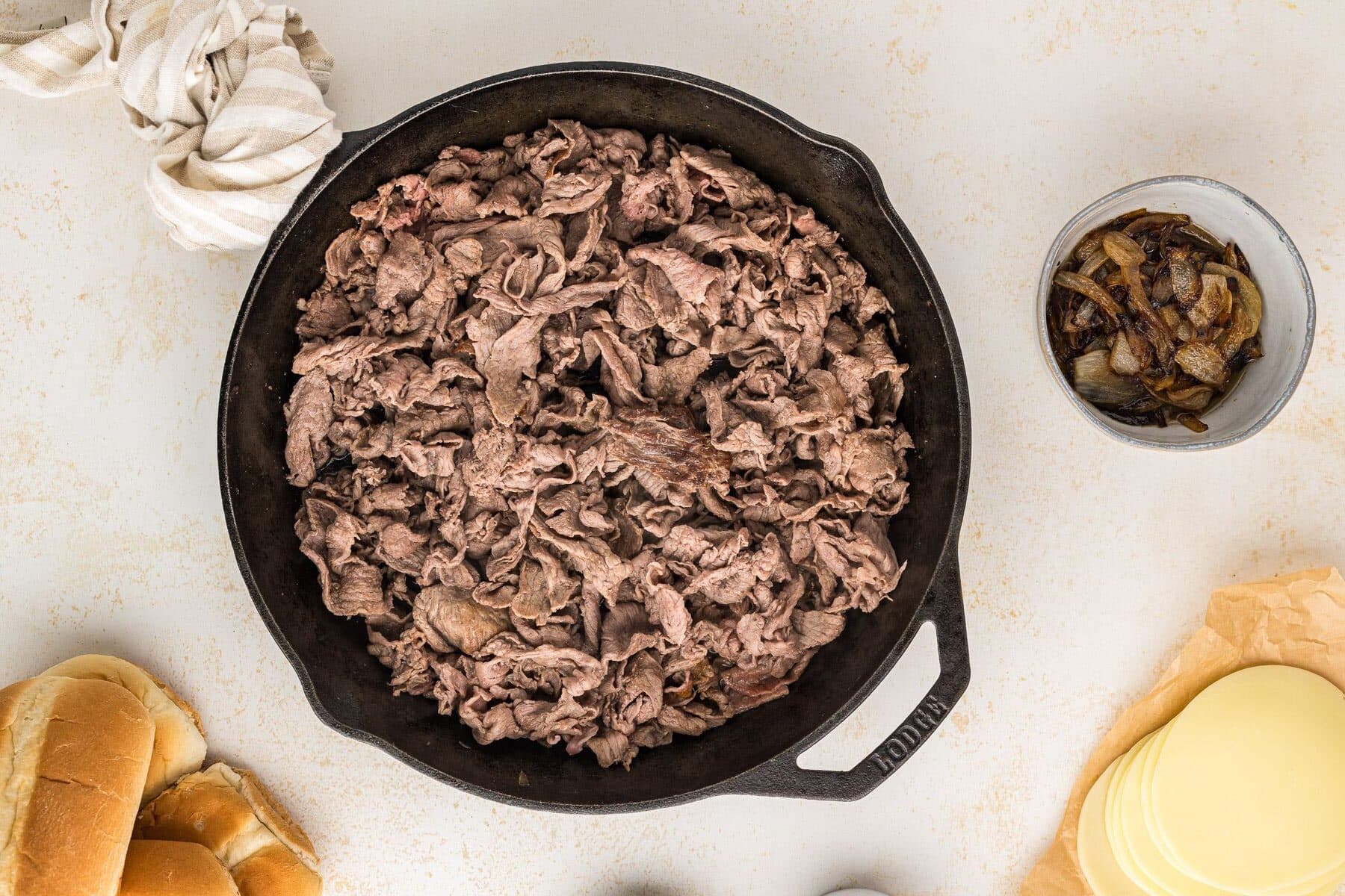 Browned shaved steak in cast iron skillet.