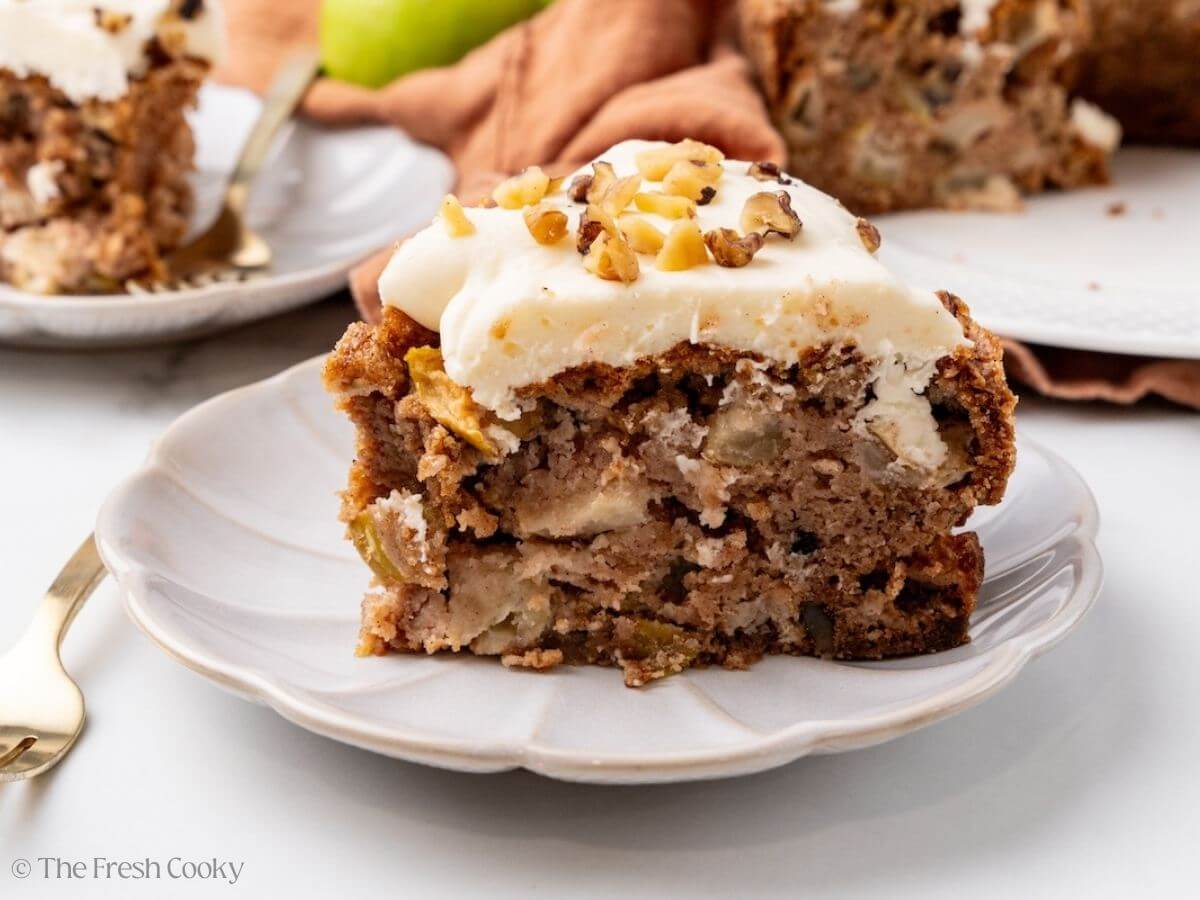 Slice of apple spice cake on a plate with frosting on top.