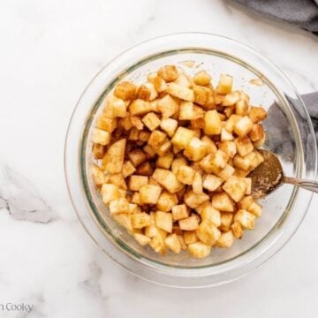 Apples in a mixing bowl combined with sugar and spices.