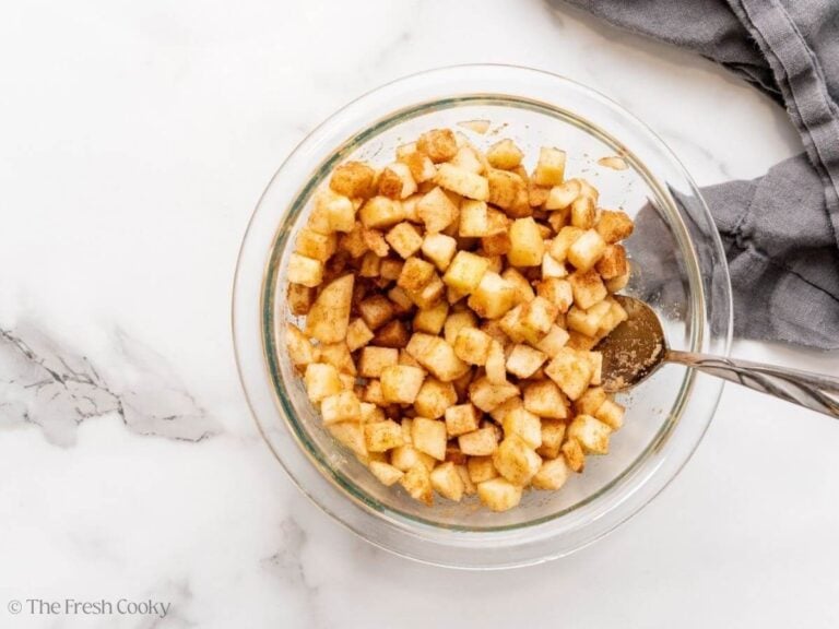 Apples in a mixing bowl combined with sugar and spices.