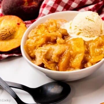 Peach cobbler served in a bowl with a scoop of vanilla ice cream.