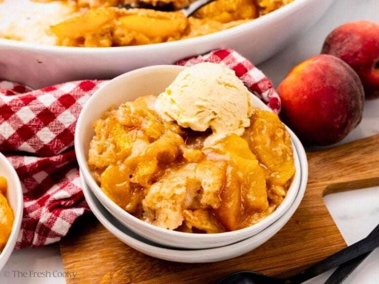 Serving of peach cobbler in a bowl with ice cream on top.