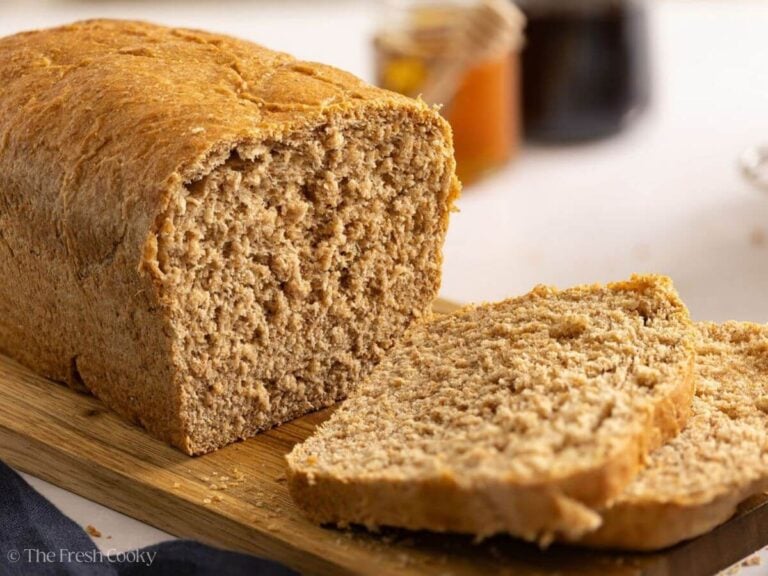 Loaf of whole wheat bread on a wooden board with two slices off the end.