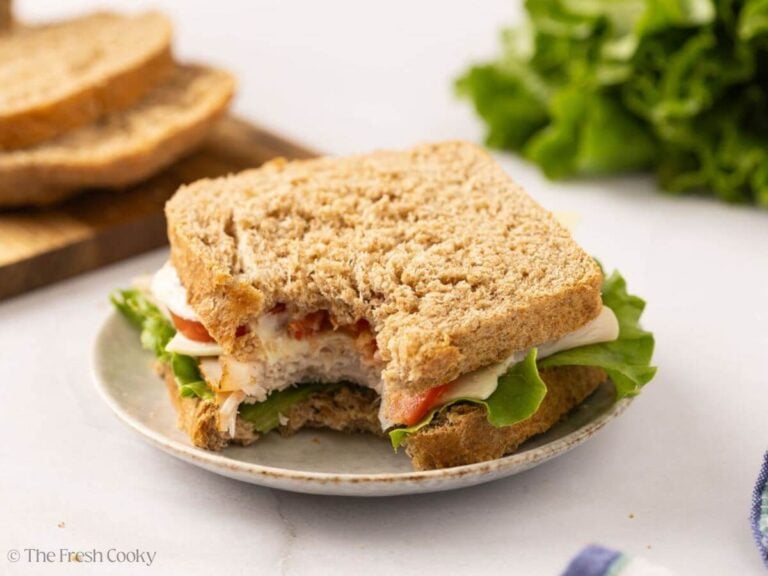 Turkey sandwich on a plate made with whole wheat bread with a bite taken from it.
