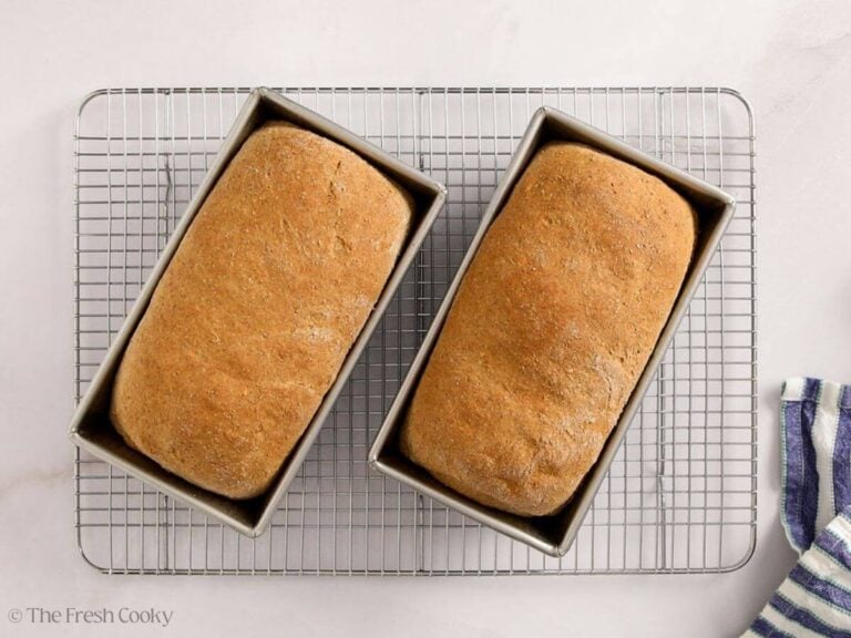 Two loaves of whole wheat sandwich bread in two loaf pans after being baked.