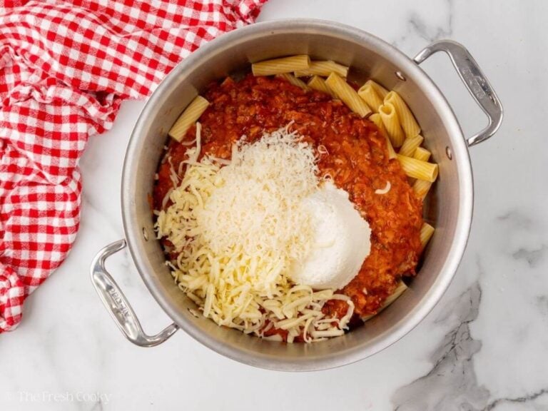 Pot with cooked pasta, tomato sauce, ricotta, parmesan and mozzarella in it before mixing.