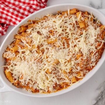 Rigatoni pasta topped with shredded mozzarella in a baking dish.
