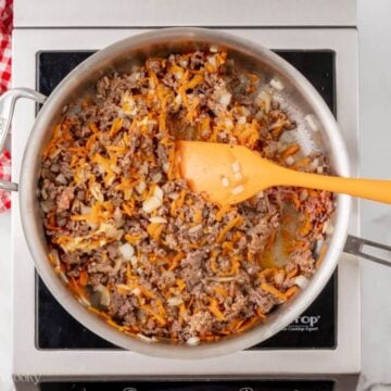 Cooked ground beef and sausage in a skillet with onions and shredded carrots.