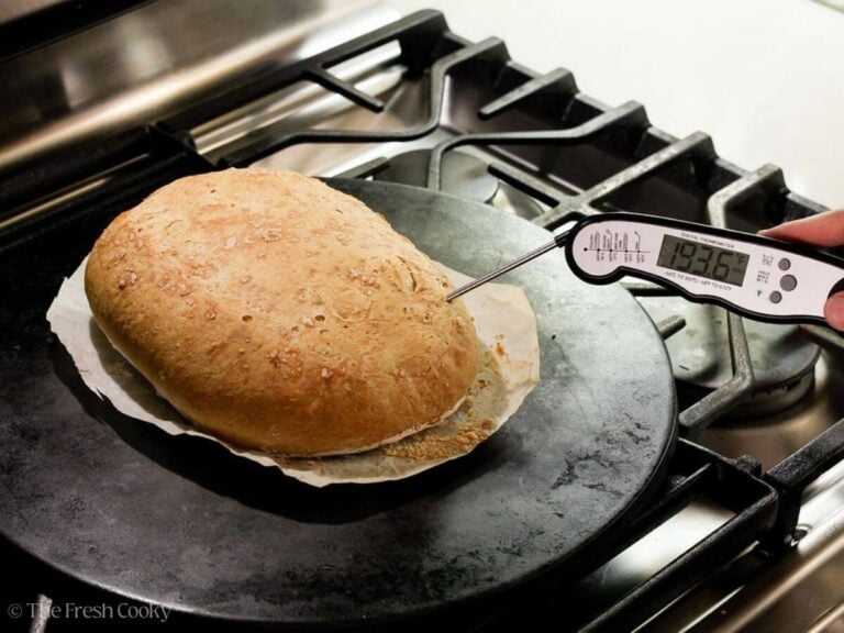 Using a thermometer to check the internal temperature of the loaf of bread.
