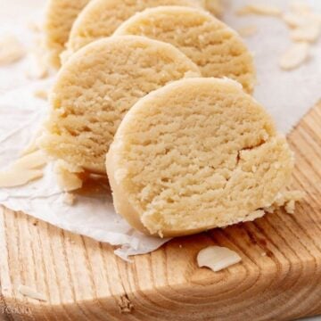 Slices of almond paste leaning against each other on a wooden board.