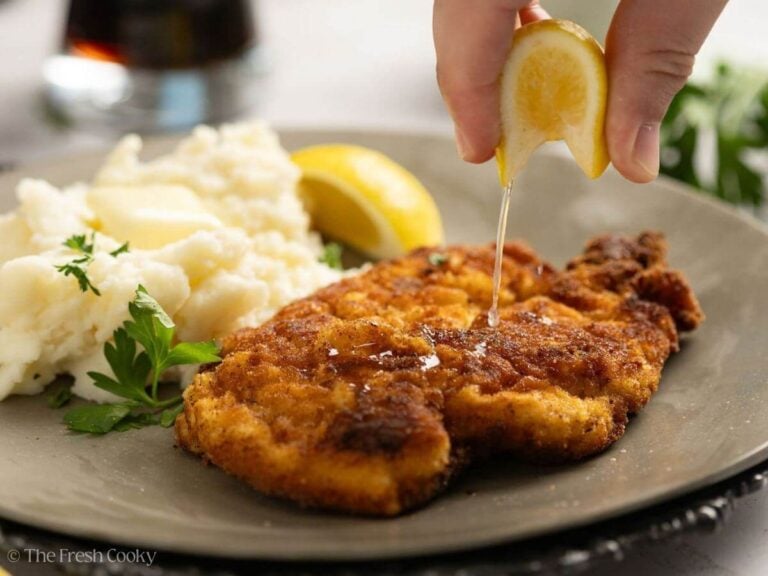 Chicken schnitzel on a plate with a hand squeezing a lemon wedge on top.