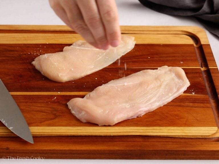Salting the sliced chicken breasts on a wooden board.