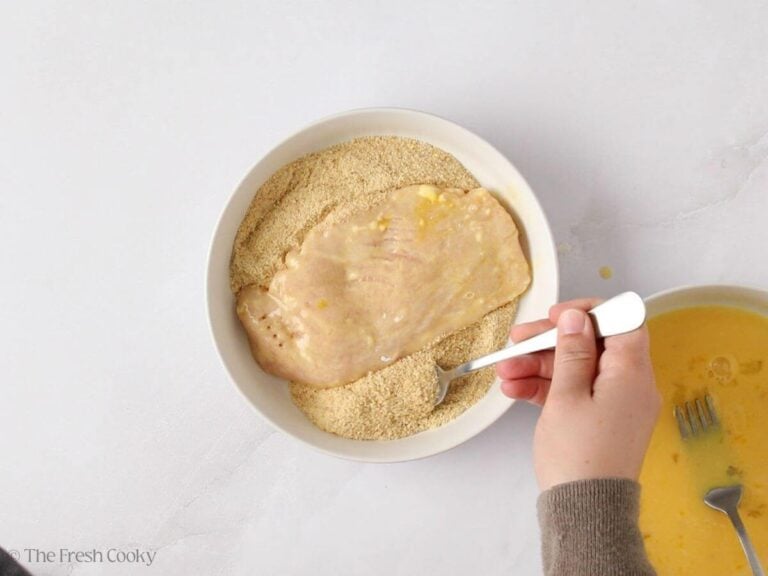Dipping the chicken in breadcrumbs to coat.