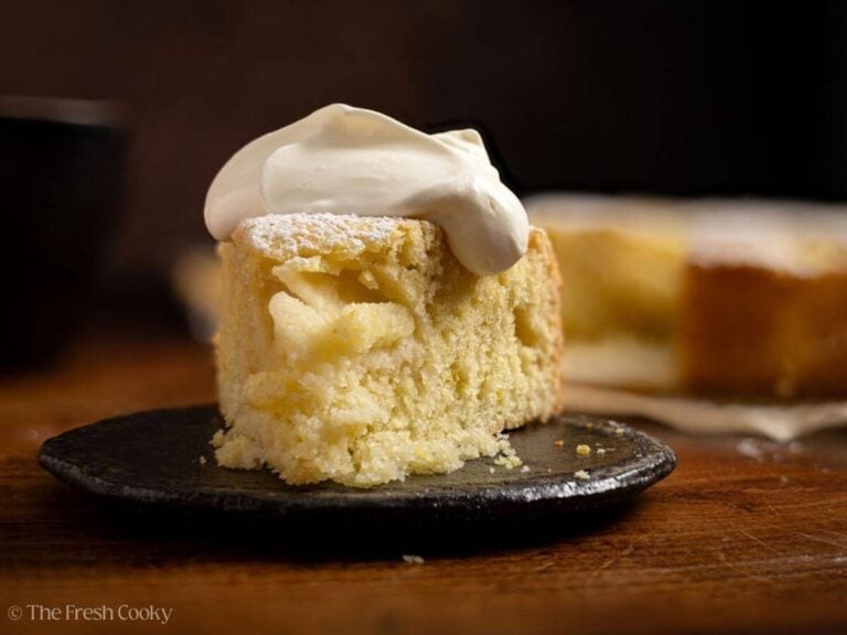 Slice of German apple cake with a dollop of lightly whipped cream on top.