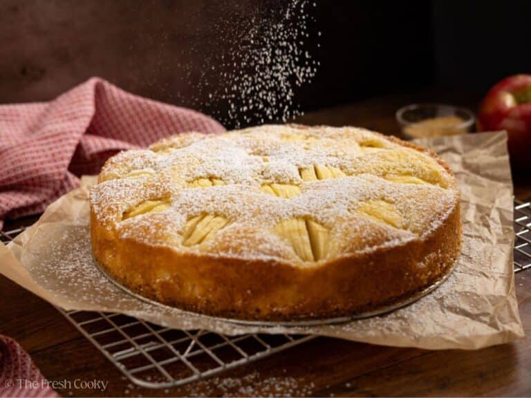 German apple cake being sprinkled with powdered sugar.