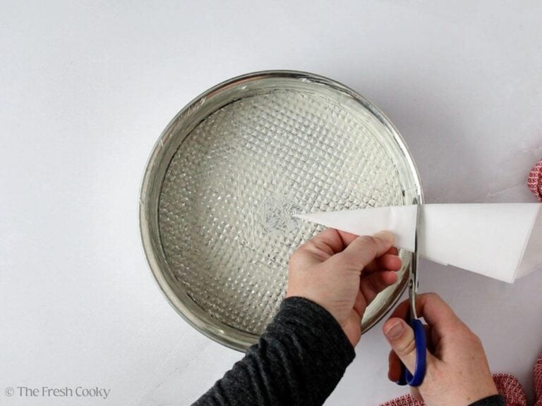 Hands cutting parchment paper into a circle to prep the cake pan.