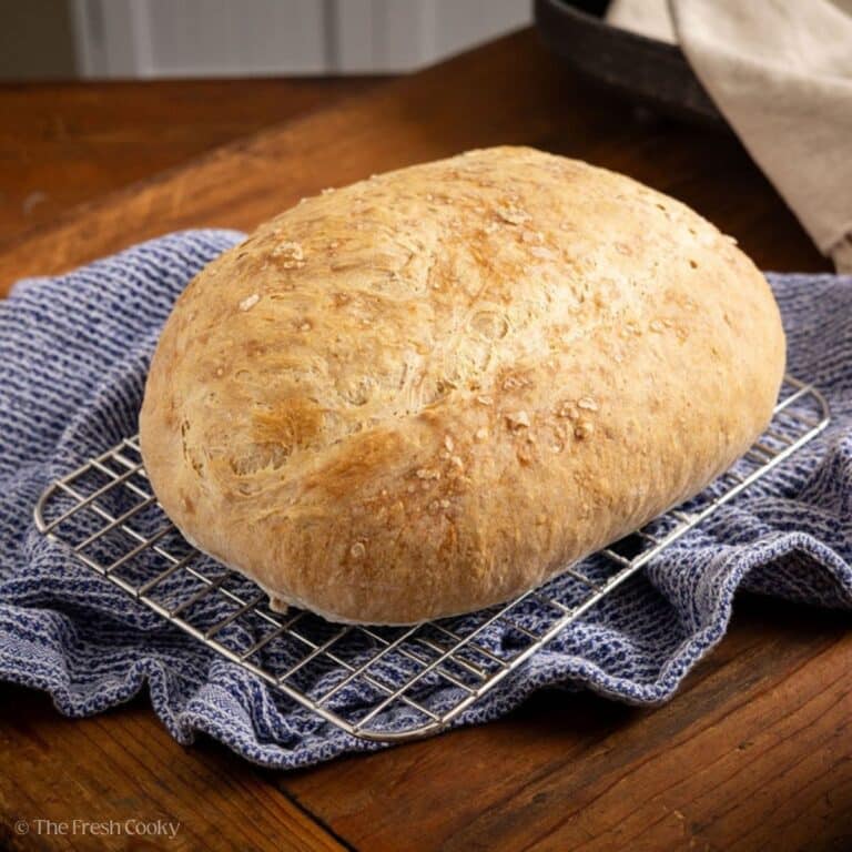 A crusty loaf of Italian artisan bread on a cooling rack.