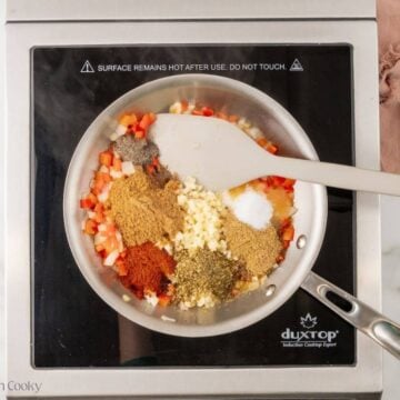 Spices and garlic added to the onion and red bell pepper in a skillet.