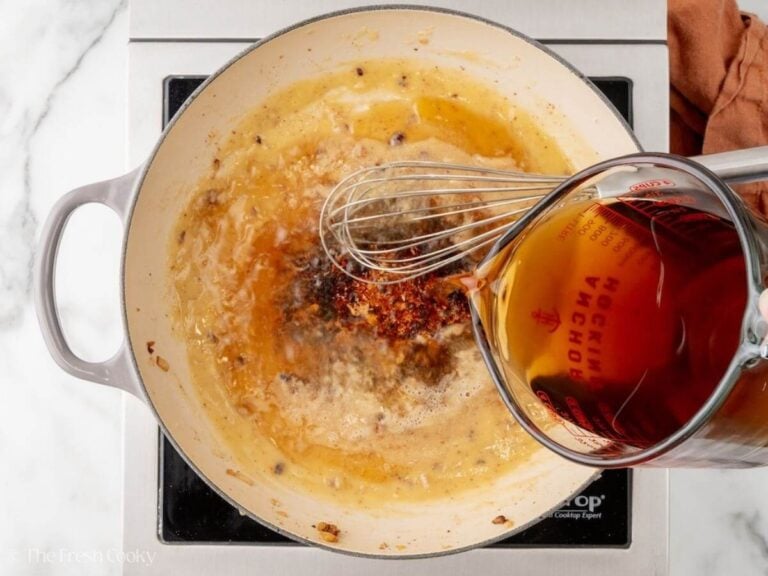 Beef broth being added to the roux in a skillet.