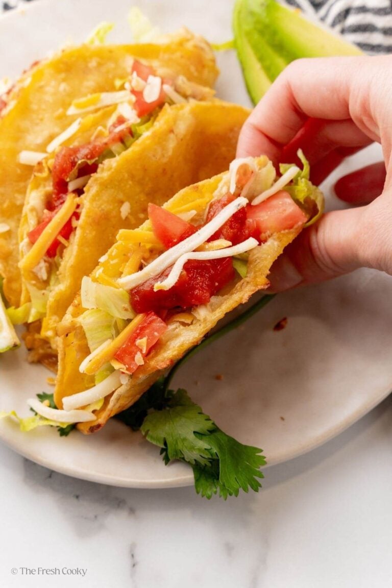 Hand picking up one of the chicken baked tacos from the plate.