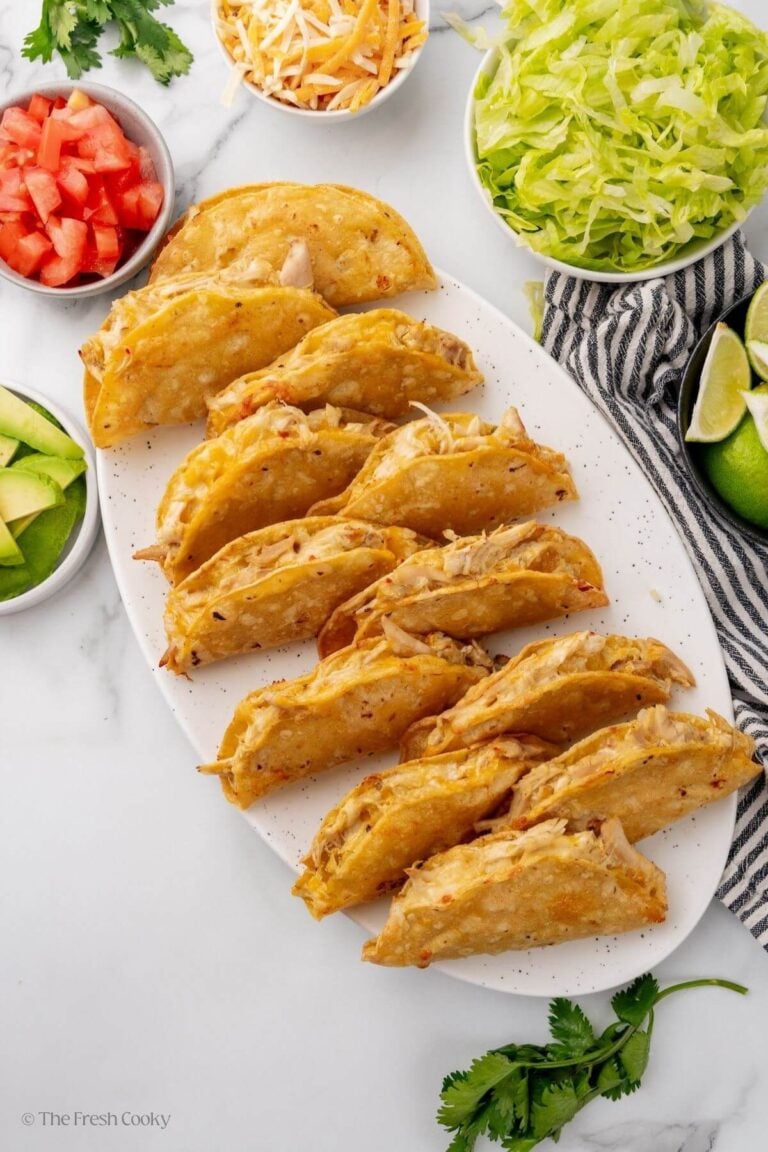 Serving platter of crunchy baked chicken tacos with toppings around them.