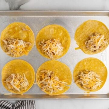 Shredded chicken mixture and shredded cheese placed on each corn tortilla.