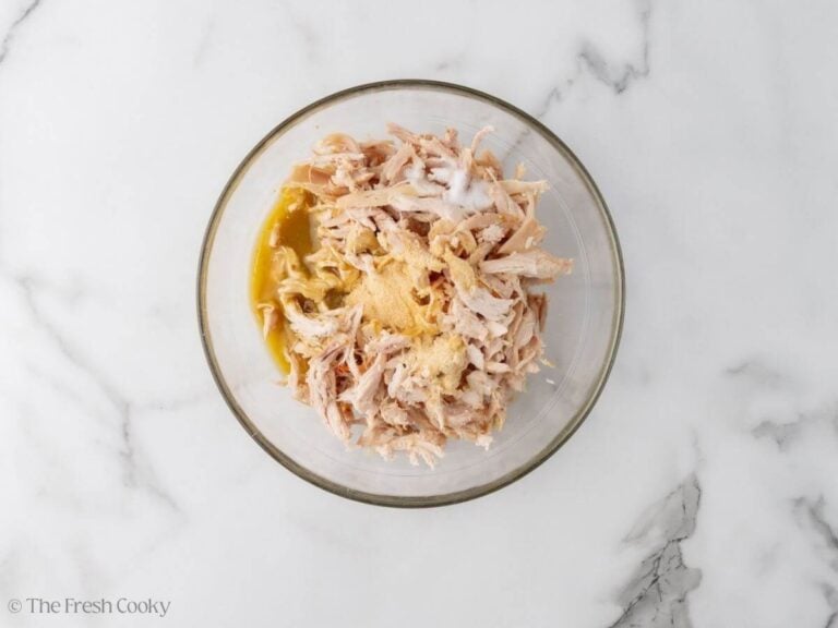 Shredded chicken in a bowl with green enchilada sauce, garlic powder, salt lime juice and onion powder.