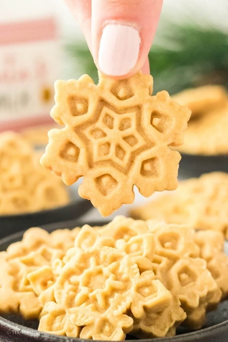 Hand holding a stamped brown sugar shortbread cookie with more below it.