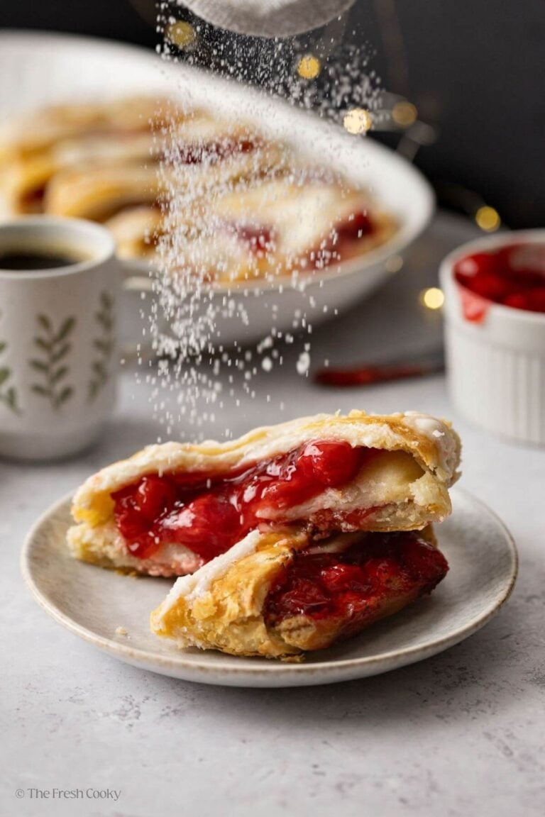 Dusting powder sugar on top of two slices of cherry Danish kringle.