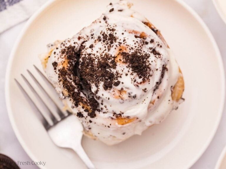 Overhead shot of a cinnamon roll on a plate with crushed Oreos on top.