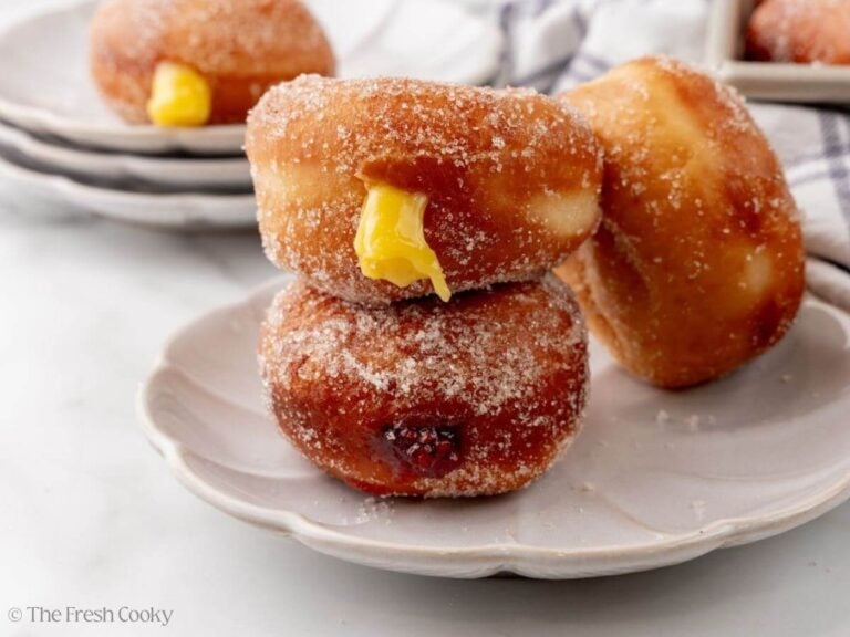 Two Polish paczki donuts stacked on a plate with one leaning on them.