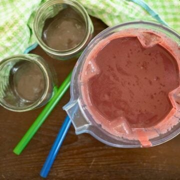 Blended vegetable and fruit smoothie next to two empty jars.