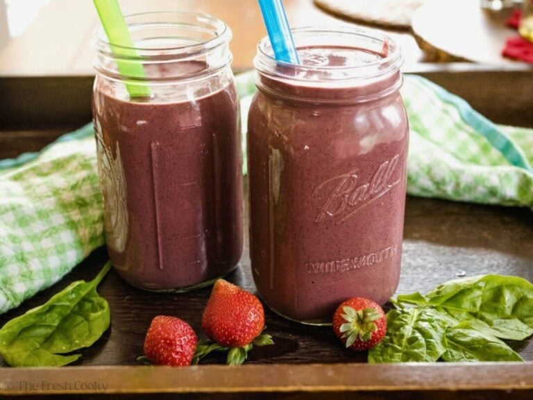 Side view of two fruit and veggie smoothies in large jars.