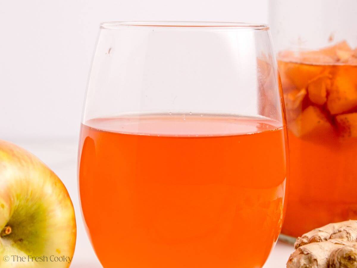 A glass of kombucha with a glass bottle of kombucha in the background. 