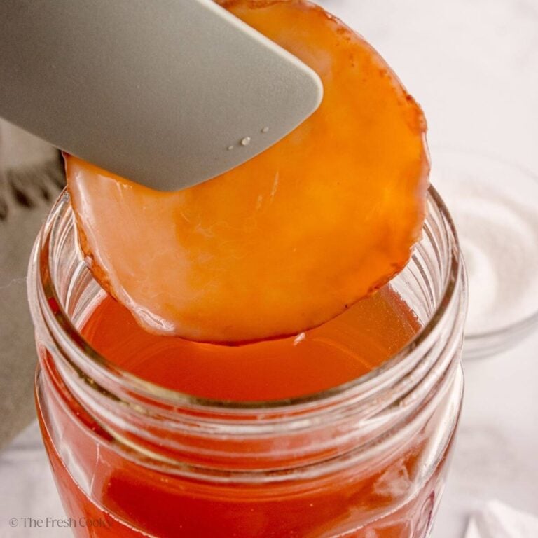 A SCOBY for kombucha is being removed from a glass jar.