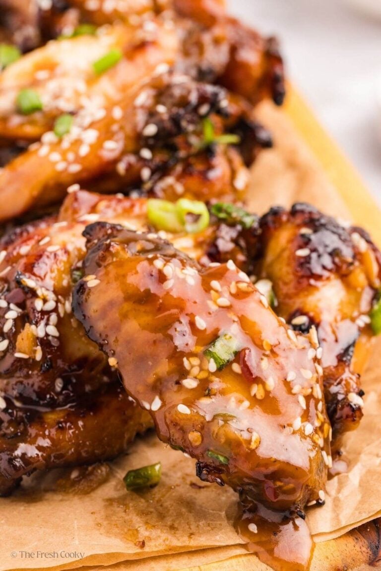 Sticky chicken wings leaning on each other served on a wooden board.