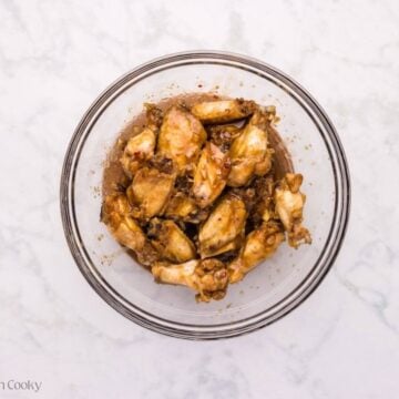 Sticky wing sauce added to the cooked wings in a mixing bowl.
