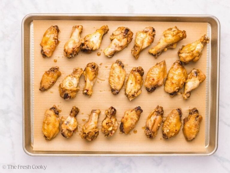 Glazed wings placed on a sheet pan lined with parchment.
