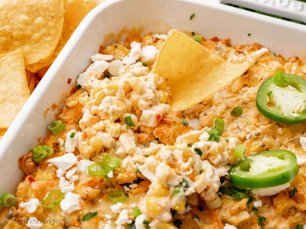 Mexican street corn dip in a white baking dish with a tortilla ship on top.