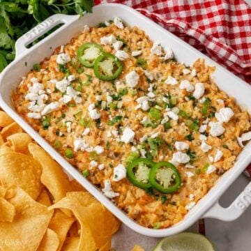 Baked Mexican street corn dip in a white baking dish, garnished with cotija cheese, jalapeño, cilantro and green onions.